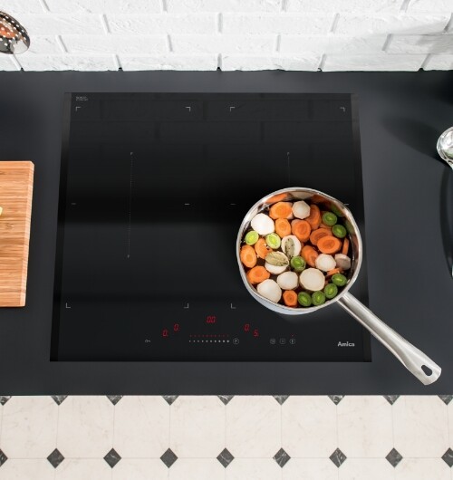 Płyta indukcyjna Amica na blacie kuchennym, na niej patelnia wypełniona warzywami