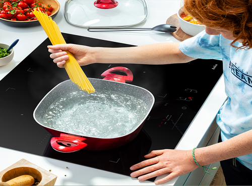 Kobieta wsypuje makaron do garnka na płycie Amica z funkcją PowerBooster, woda mocno wrze