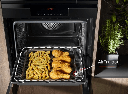 Wysunięta blacha piekarnika z frytkami i kurczakiem w panierce 