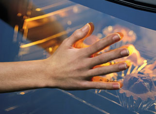 Dłoń kobiety przyciśnięta do szyby włączonego piekarnika